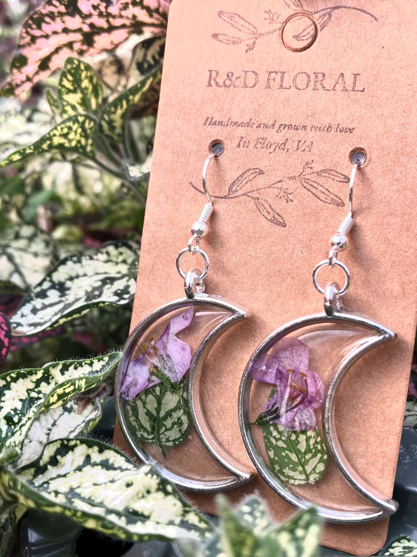 Silver moon shaped earrings with polka dot plant leaves and Bacopa flowers encased in resin by R & D Floral.
