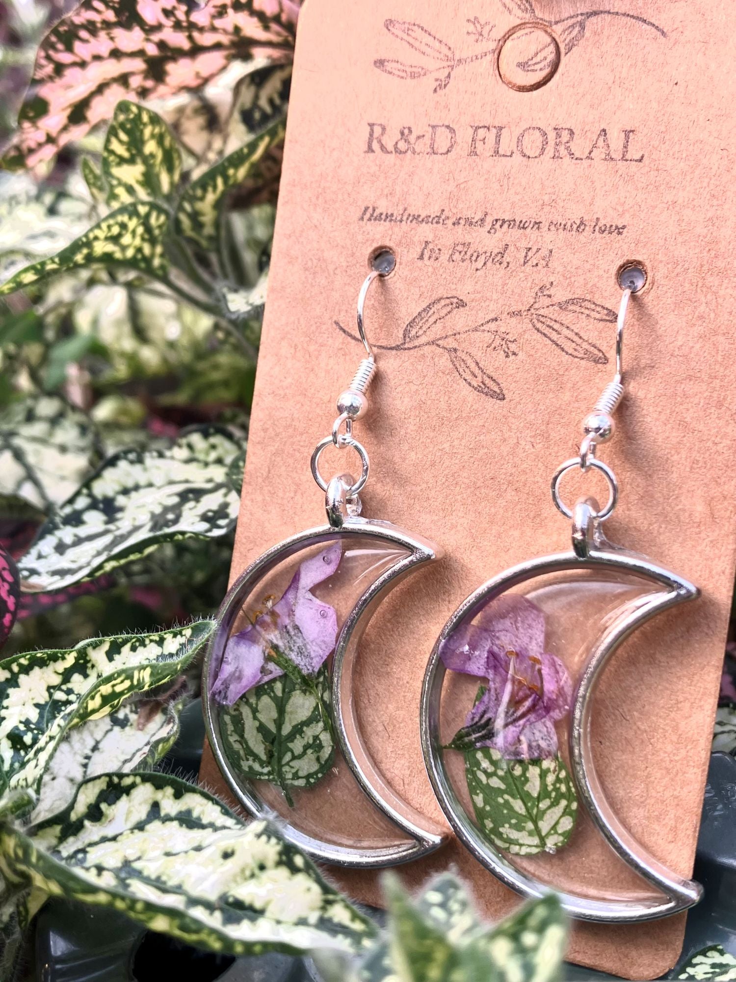 Silver moon shaped earrings with polka dot plant leaves and Bacopa flowers encased in resin by R & D Floral.