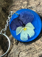 Keychain with a blue background featuring a pressed flower on a wooden surface