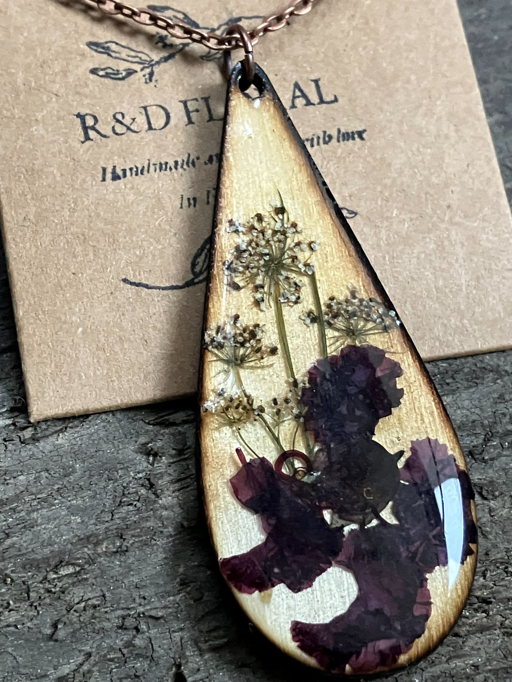 Teardrop wooden pendant with real Crape Myrtle and Queen Anne’s Lace encased in resin, available on silver or cord chain, handmade by R&D Floral.