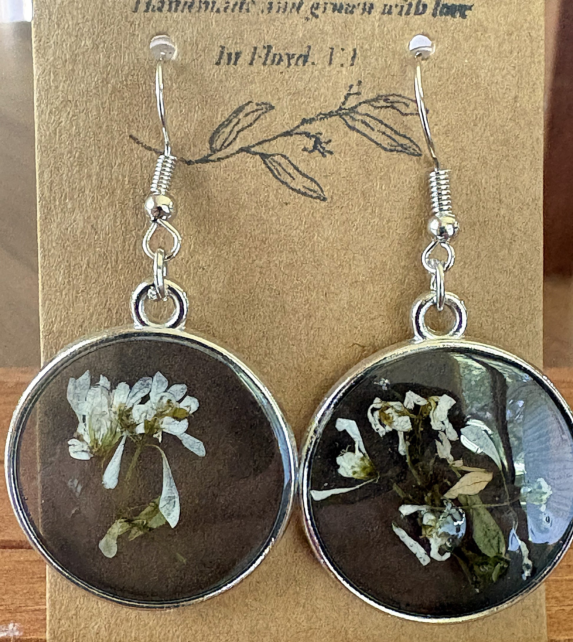 Black and white pressed Euphorbia earrings in round silver metal bezels with resin dome, on a Handmade in Floyd VA kraft card