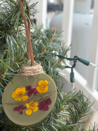 Close-up of buttercup and verbena pressed flower ornament in sage green resin