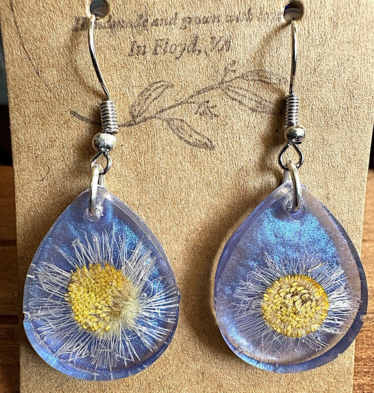Front view of blue shimmer teardrop resin earrings on display card with pressed daisy inside