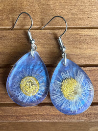 Blue real pressed daisy teardrop resin earrings laid flat on wood surface, front view