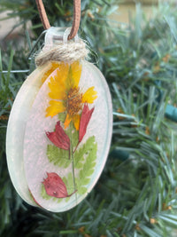 Close-up of fern, Salvia, and Coreopsis pressed flower ornament in iridescent resin