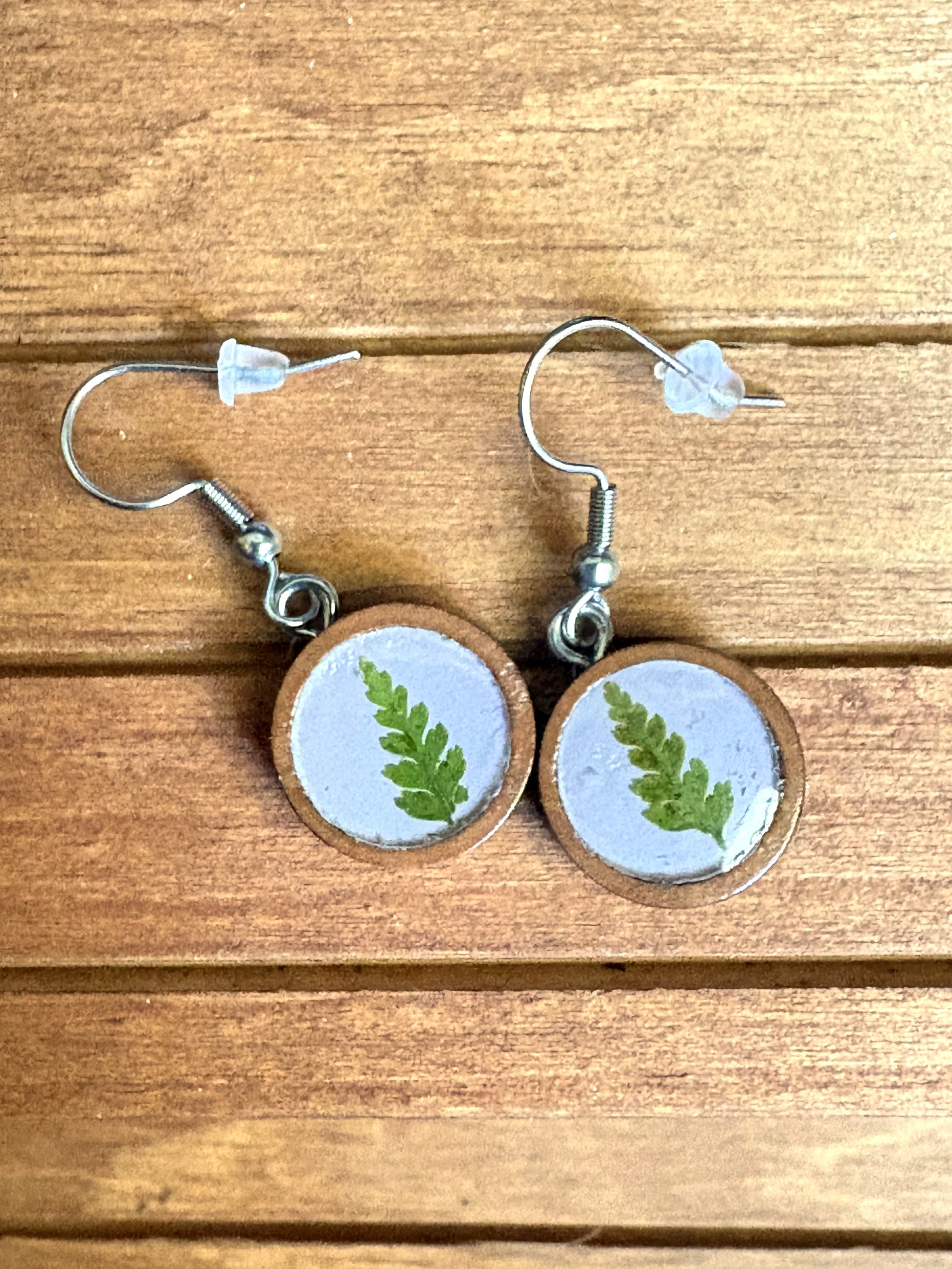 Handmade wooden dangle earrings with pressed green fern leaf in lavender resin, side view on wood surface