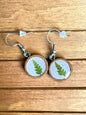 Handmade wooden dangle earrings with pressed green fern leaf in lavender resin, side view on wood surface
