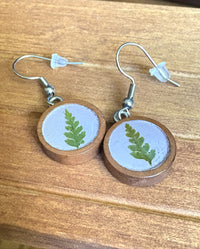 Pair of round walnut wood earrings with green fern pressed in light purple resin, front view