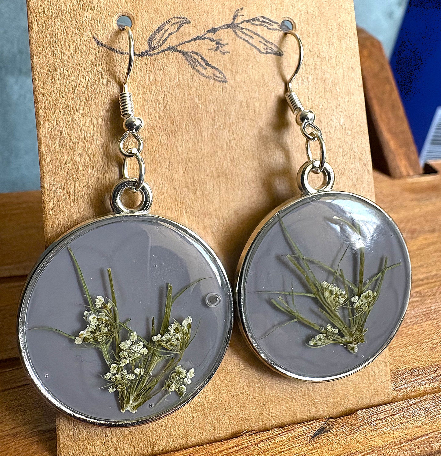 Grey resin round earrings with pressed Queen Anne's Lace flowers displayed on wooden earring card