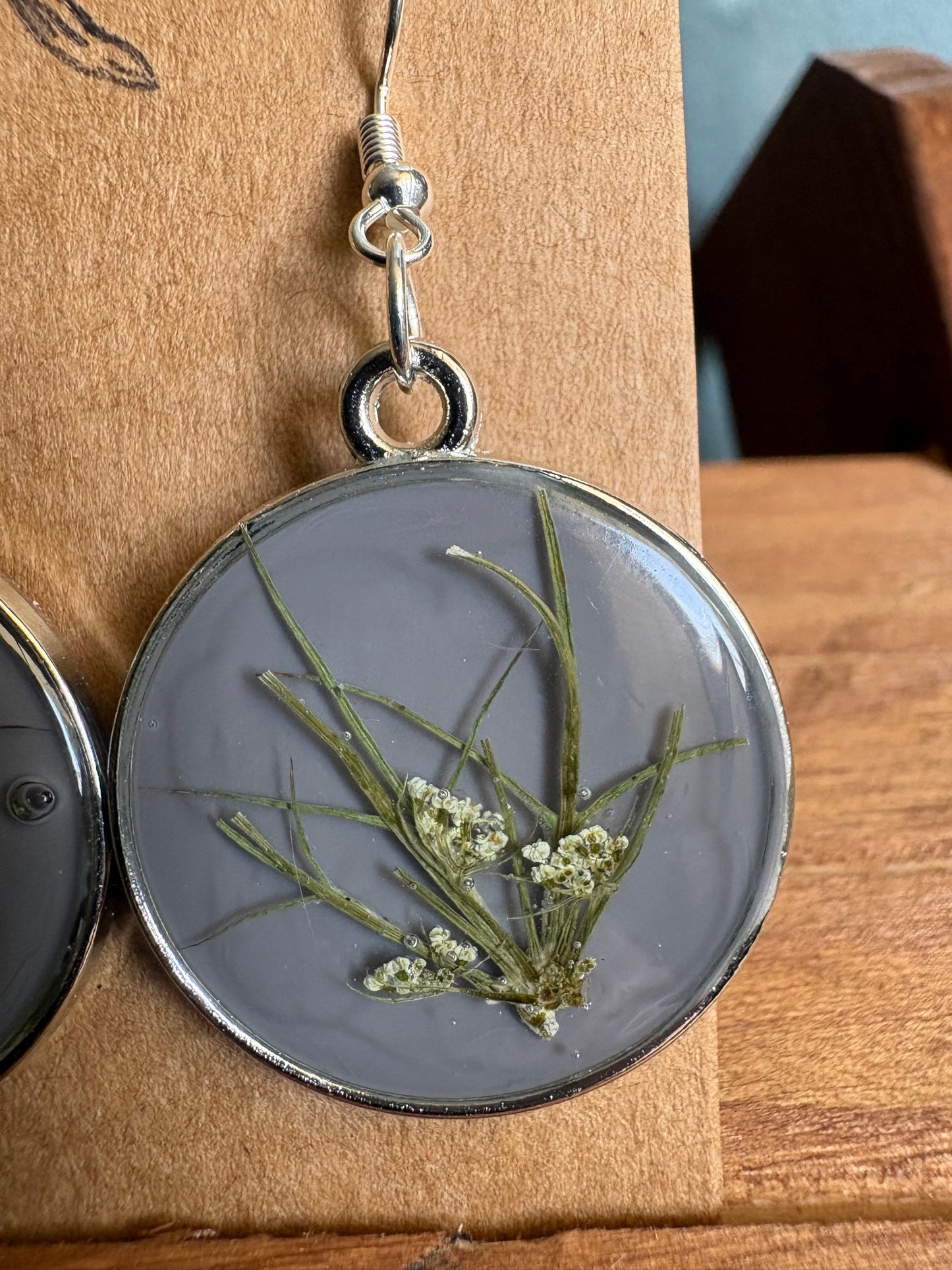 Close-up of grey resin round earring showing pressed botanical stems and Queen Anne's Lace flowers