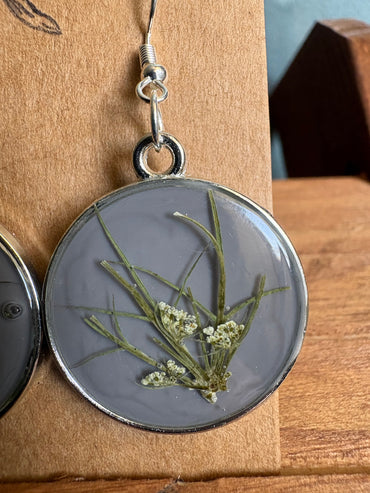 Close-up of grey resin round earring showing pressed botanical stems and Queen Anne's Lace flowers
