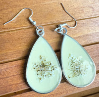 Light Yellow Metal Queen Anne's Lace Earrings flat lay on wood, showing pressed botanical detail in light yellow resin teardrop