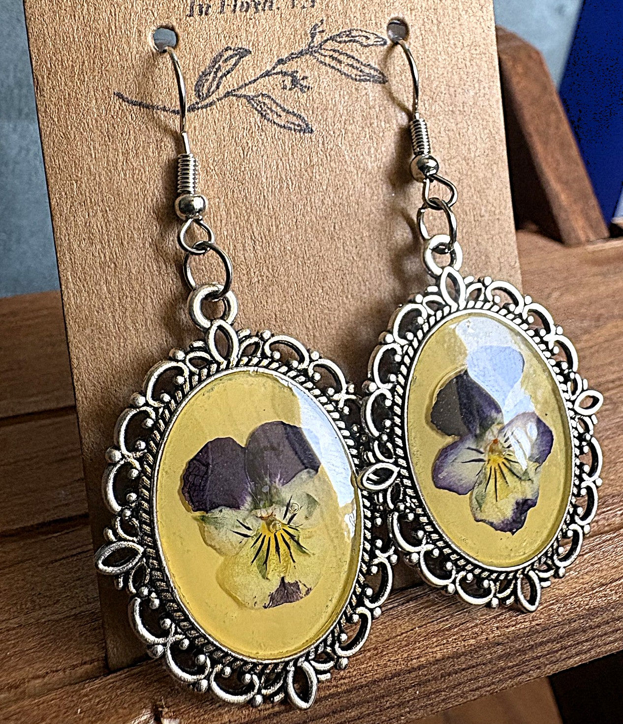 Viola Victorian metal earrings on display card showing pressed purple viola flowers in yellow resin with ornate silver filigree frame