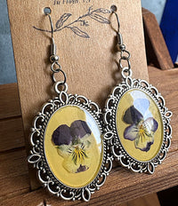 Viola Victorian metal earrings on display card showing pressed purple viola flowers in yellow resin with ornate silver filigree frame