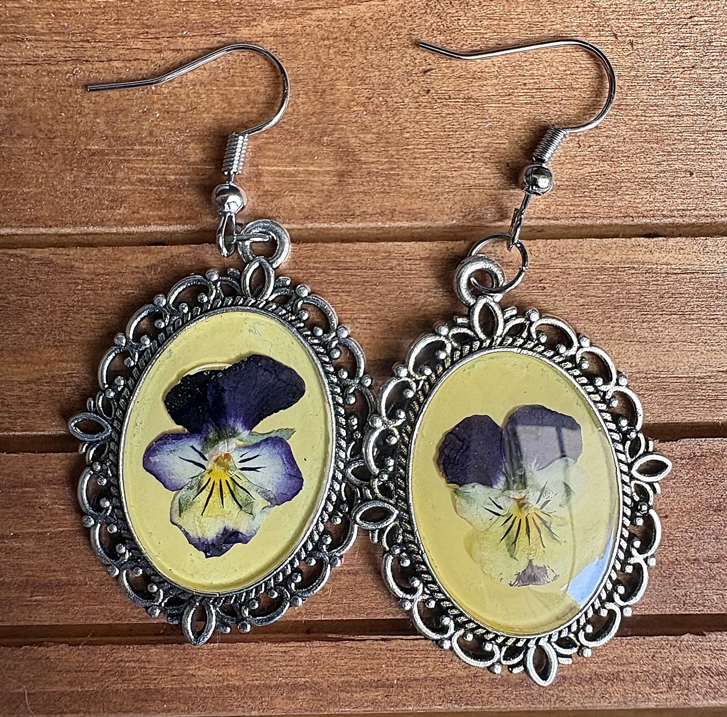 Viola Victorian earrings flat on wood surface showing pressed purple and white viola blooms in yellow resin