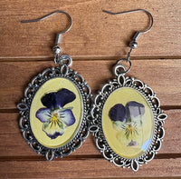 Viola Victorian earrings flat on wood surface showing pressed purple and white viola blooms in yellow resin