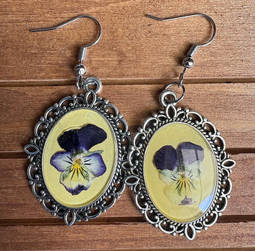 Viola Victorian earrings flat on wood surface showing pressed purple and white viola blooms in yellow resin