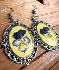 Angled view of viola Victorian metal earrings with ornate silver filigree frame and fish hook wires
